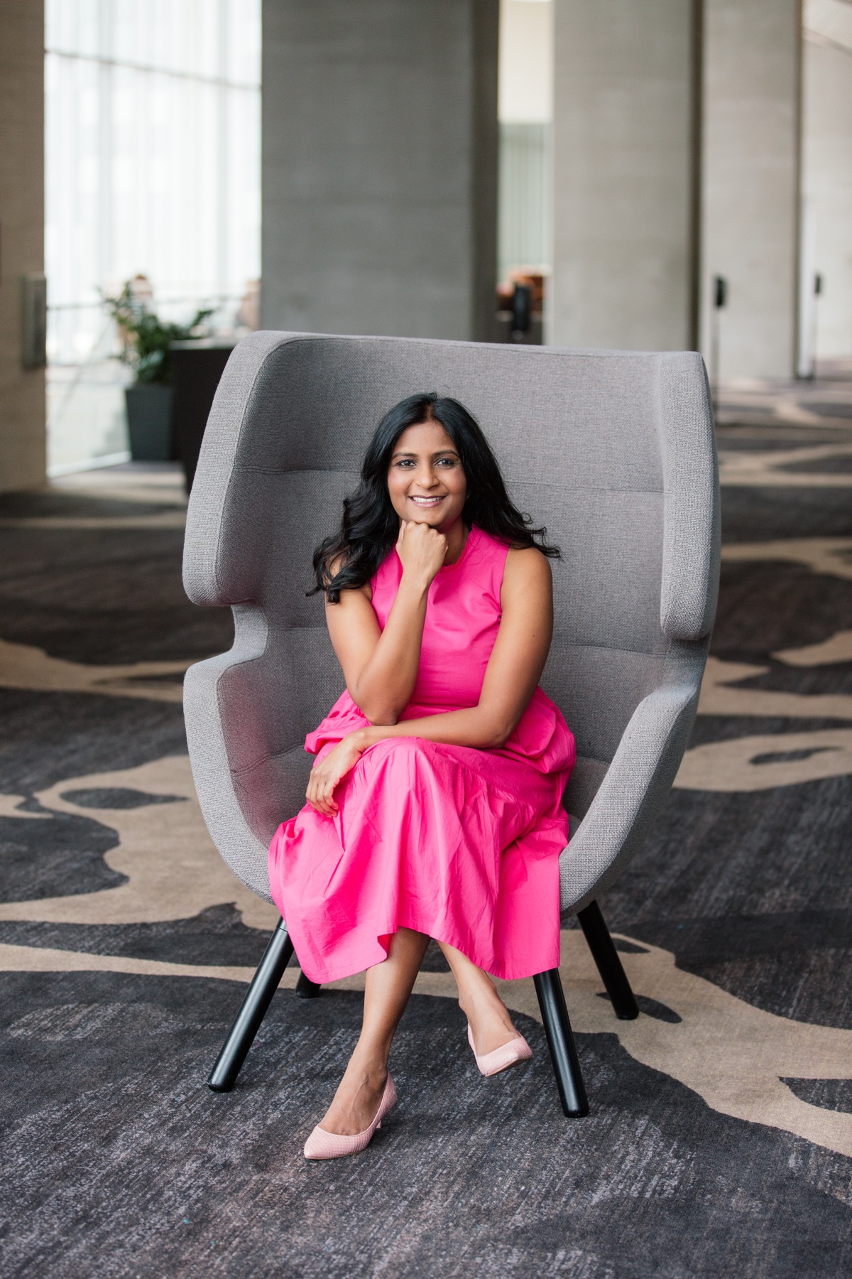 Sapna Rad seated in a chair wearing a bright pink dress